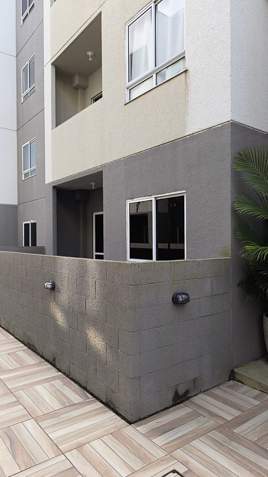 Fachada lateral do prédio com paredes texturizadas em tons de cinza e bege, janelas e piso cerâmico amadeirado.